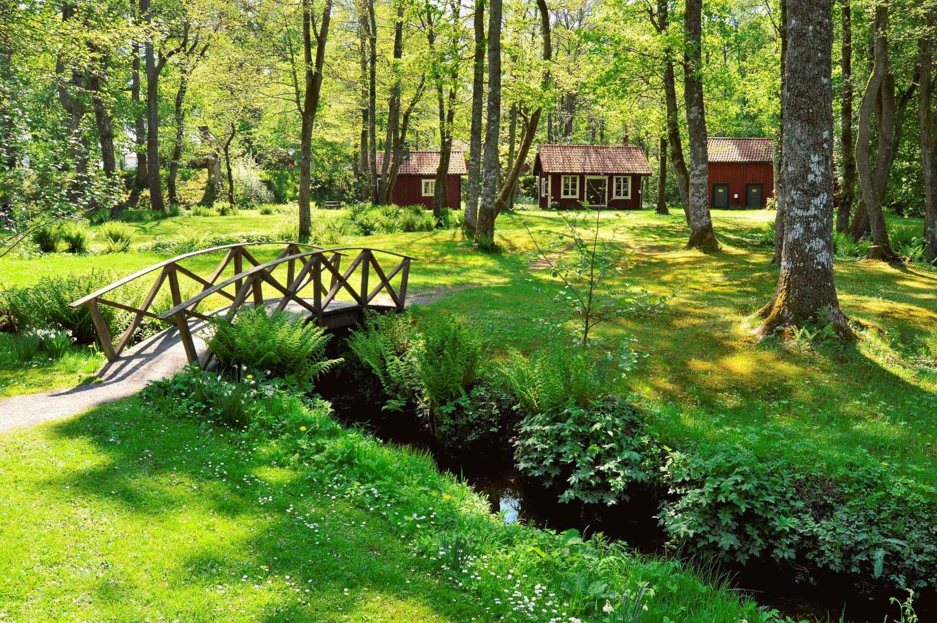 Beautiful summer landscape featuring a wooden bridge and red cabins in Swedish countryside.
